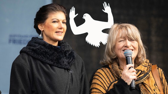 Sahra Wagenknecht und Alice Schwarzer auf der sogenannten Friedensdemo in Berlin. Dahinter eine sich ergebende Friedenstaube. (extra 3 vom 02.03.2023 im Ersten) © NDR 