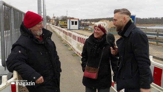 Philipp Jess steht mit einem älteren Ehepaar auf der Brücke und interviewt sie. © Screenshot 