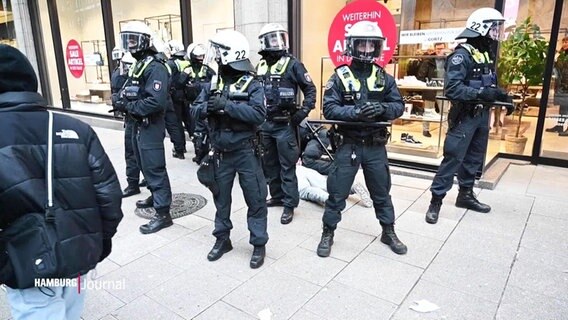 Polizistinnen in Kampfmontur stehen vor einem Geschäft. Im Hintergund liegt ein Mensch auf dem Boden. © Screenshot 