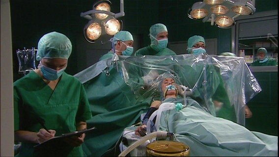 Mehrere Ärzte stehen in einem OP-Saal. © Screenshot 