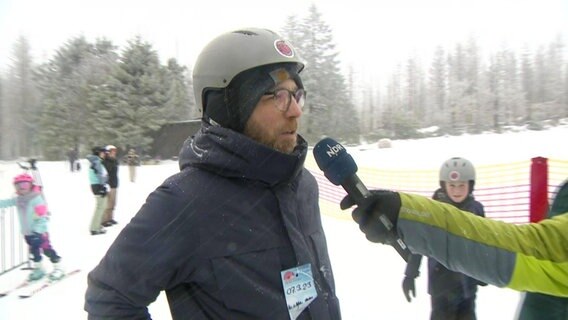 Ein Tourist wird neben einer Skipiste interviewt. © Screenshot 