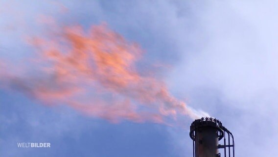 Aus einem Fabrikschornstein lodert eine orange Flamme. © Screenshot 
