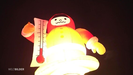 Eine mit Luft gefüllte Maskottchenfigur mit einem Termometer im Arm und verfrorenem Gesichtsausdruck. © Screenshot 