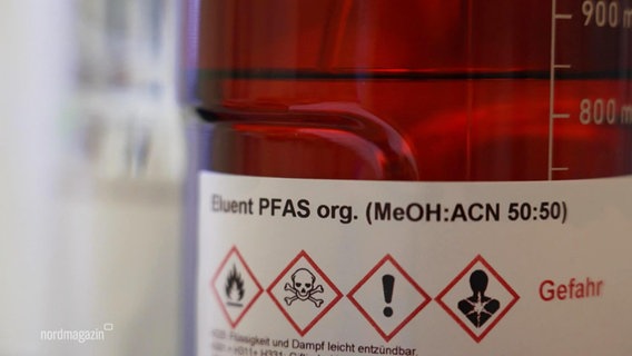 Eine braune Glasflasche mit einer transparenten Flüssigkeit. Auf dem Etikett steht der Name "PFAS", darunter vier Gefahrenhinweise, unter anderem das Symbol eines Totenkopfes. © Screenshot 