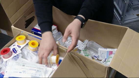 Hände, die Medikamente und Verbandsmaterial in Kartons packen. © Screenshot 