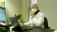 Eine Person in Kittel und mit FFP 2 Maske bedient einen Laptop © Screenshot 
