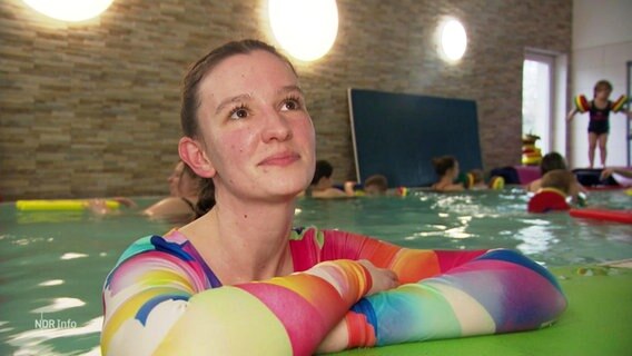 Person mit buntem Oberteil in einem Schwimmbecken mit Kindern im Hintergrund © Screenshot 