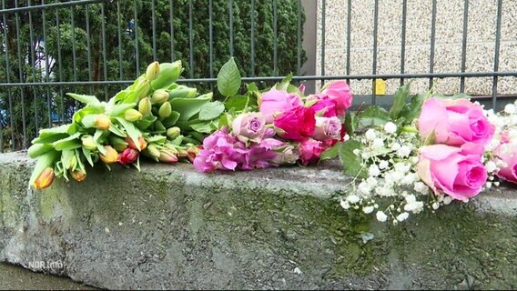 Auf einer Mauer liegen mehrere Sträuße Blumen. © Screenshot 