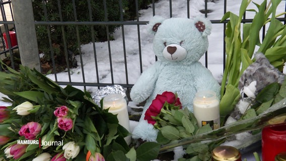 Ein Teddybär zwischen Blumen und Kerzen im Schnee. © Screenshot 