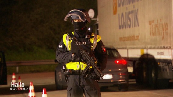 Ein Polizist mit Maschinengewehr steht auf einem Autobahn-Parkplatz. © Screenshot 