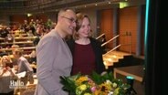 Die neuen Landesvorsitzenden Greta Garlichs und Alaa Alhamwi stehen Arm in Arm mit einem Blumenstrauß für ein Foto. © Screenshot 