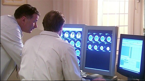 Zwei Ärzte schauen auf einen Monitor mit Aufnahmen von einem Gehirn. © Screenshot 