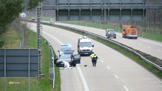 Ein schwarzes Auto wird von der Polizei auf der Autobahn untersucht. © Screenshot 