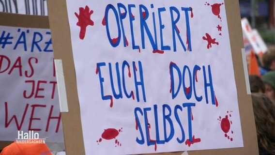 Ein Schild auf einer Demo mit der Aufschrift: "Operiert euch doch selbst" © Screenshot 