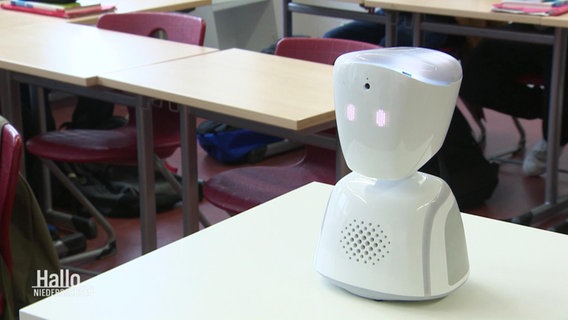 Ein kleiner weißer Roboter steht auf einem Tisch in einem Klassenzimmer © Screenshot 