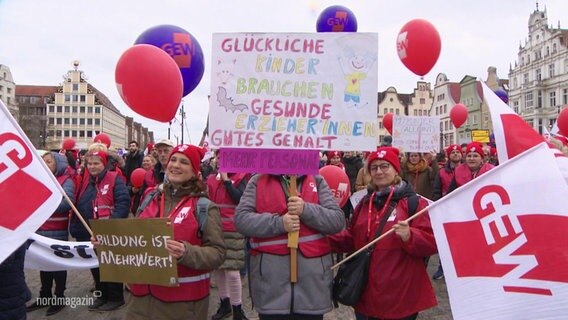 Menschen halten Schilder auf einer Demonstration und fordern bessere Bedingungen für Kitas. © Screenshot 