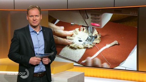 Moderator Thilo Tautz, im Hintergrund eine Bild von einer Nähmaschine mit einem Stück Stoff, aus dem ein Löwe genäht wird. © Screenshot 