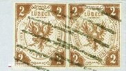 Zwei alte, sich ähnelnde Lübecker Briefmarken. Auf ihnen ist ein zweiköpfiger bräunlicher Adler abgebildet. © Screenshot 