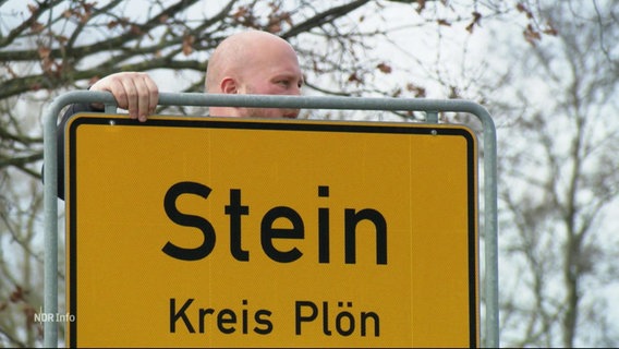 Mann befestigt ein Ortsschild in "Stein". © Screenshot 