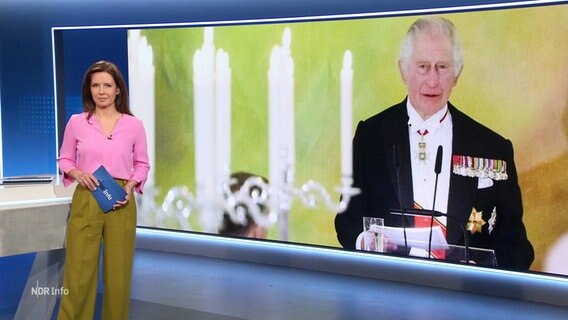 Romy Hiller moderiert die 17 Uhr Ausgabe NDR Info. Im Hintergrund ist ein Foto von König Charles bei seinem Staatsbesuch im Bundestag zu sehen. © Screenshot 
