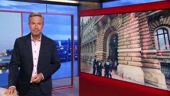 Thomas Görlitzer moderiert die Frühausgabe Hamburg Journal. Im Hintergrund ist ein Foto von Aktivisten, die das Hamburger Rathaus besprühen zu sehen. © Screenshot 