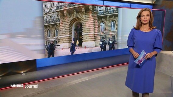 Julia Niharika Sen moderiert die Spätausgabe Hamburg Journal. Im Hintergrund ist ein Foto der beschmierten Rathausfassade zu sehen. © Screenshot 