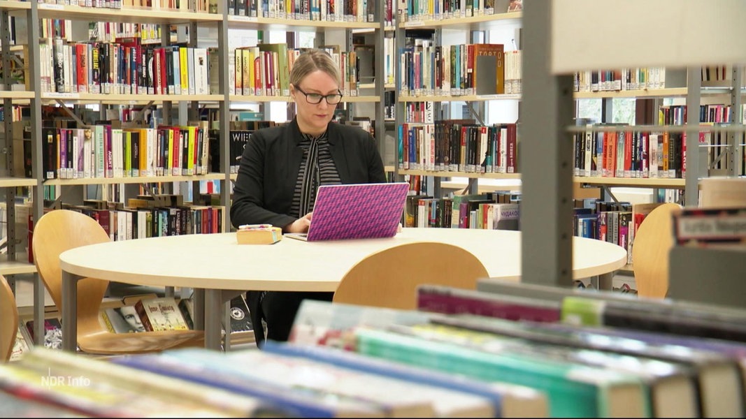 Professorin Jennifer Henke sitzt in einer Bibliothek am Laptop.