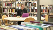 Professorin Jennifer Henke sitzt in einer Bibliothek am Laptop. © Screenshot 