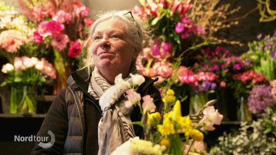 Florisatin Svenja Barg steht in ihrem Blumengeschäft und blickt zufrieden in die Höhe. © Screenshot 