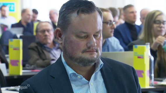Der FDP-Politiker René Domke sitzt mit herabgesenktem Blick auf dem Landesparteitag der FDP in Mecklenburg-Vorpommern. © Screenshot 