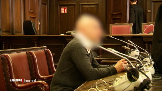 Ein Angeklagter sitzt auf der Anklagebank in einem Gerichtssaal. Sein Gesicht ist unkenntlich gemacht. © Screenshot 