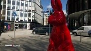 Eine rot lackierte Statue eines Hasen steht auf einem Platz in derHamburger Innenstadt. © Screenshot 