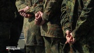Mehrere Einsatzkräfte der Bundeswehr stehen in Reihe und haben ihre Arme auf dem Rücken verschränkt. © Screenshot 