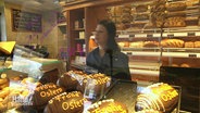 Eine Bäckerin hinter ihrer Ladentheke, Backwaren im Vordergrund. © Screenshot 