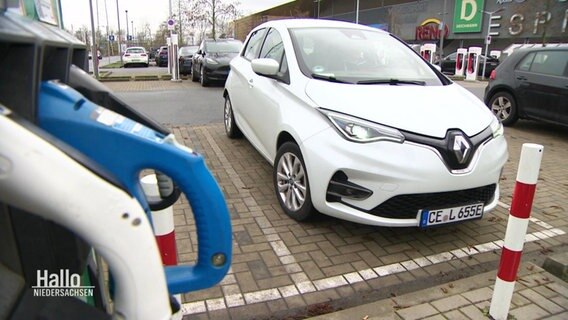 Ein weißes E-Auto parkt auf einem Parkplatz an einer Ladesäule. © Screenshot 