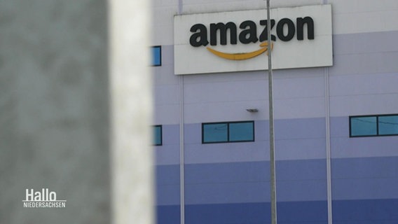 Blick aus der Ferne auf eine Fassade eines Logistikzentrums an der ein großes Amazon-Logo prangt. © Screenshot 