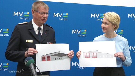 Ministerpräsidentin Manuela Schwesig hällt zusammen mit einem Mann in Feuerwehruniform Skizzen des geplanten Baus eines Feuerwehrwache hoch. © Screenshot 