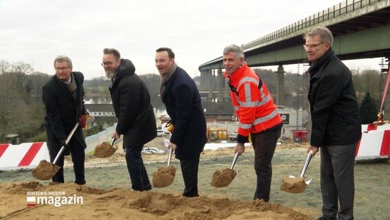 Politiker und Bauarbeiter halten Spaten bereit beim Spatenstich der Rader Hochbrücke. © Screenshot 