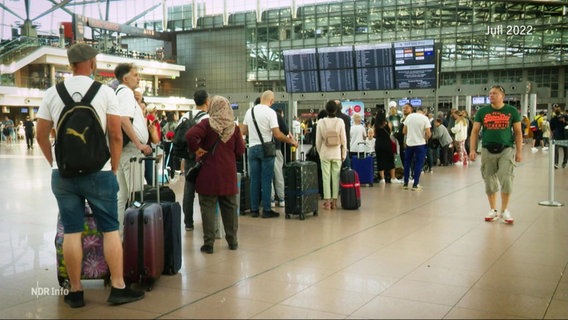 Viele Abreisende stehen in der Terminalhalle des Hamburger Flughafen mit ihren Gespäckstücken in einer langen Schlange. © Screenshot 