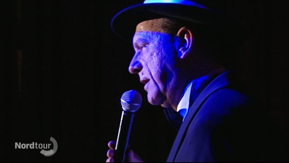 Der Sinatra-Tribut-Sänger Jens Sörensen bei einem Auftritt auf der Bühne in blauem Licht. © Screenshot 