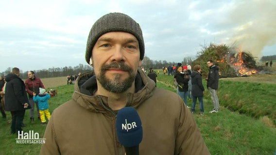 Reporter Janek Wiechers steht auf einer Wiese, hinter ihm ein Osterfeuer. © Screenshot 