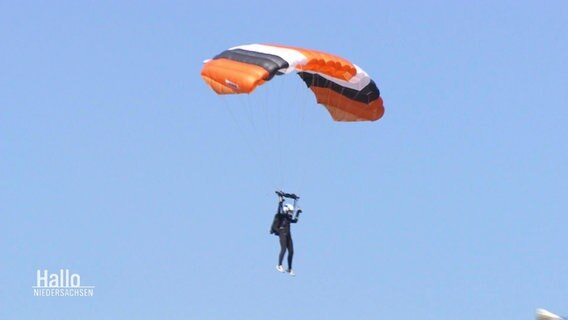 Eine Frau fliegt an einem Fallschirm durch die Luft. © Screenshot 