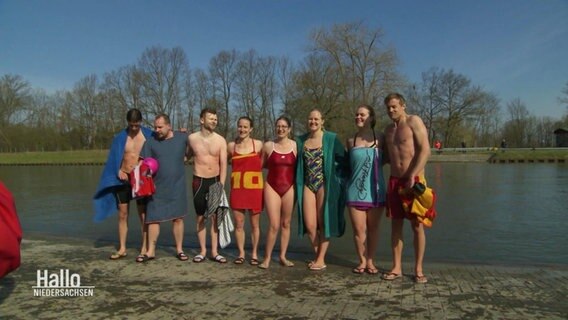 Mehrere Personen in Badekleidung posieren auf einem Steg an einem Kanal für ein Gruppenfoto. © Screenshot 