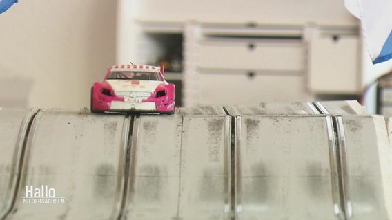 Ein Slot-Car einer Carrera-Bahn fährt in seiner Fahrrinne über einen Hügel in dem Streckenabschnitt. © Screenshot 