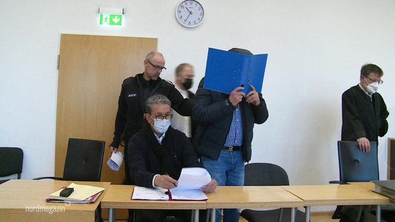 Ein in erster Instanz verurteilter Frauenmörder schützt sein Gesicht mit einem Aktenordner. © Screenshot 