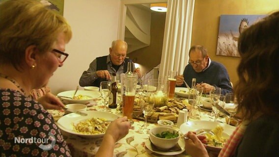 Mehrere Personen sitzen an einem kreisrunden Esstisch und essen gemeinsam. © Screenshot 