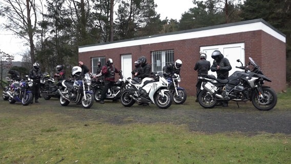 Mehrere Motorradfahrende stellen ihre Räder vor einem kleineren Bungalow ab. © Screenshot 