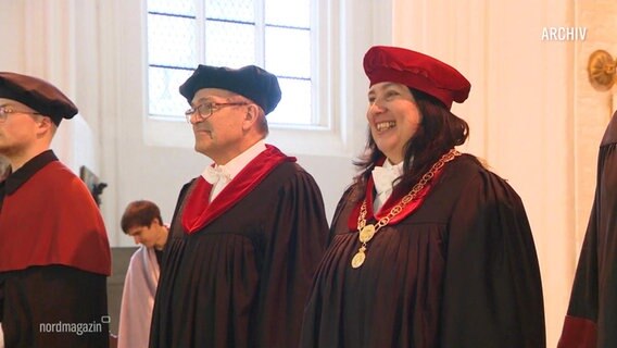 Der ehemalige Direktor der Uni Rostock Wolfgang Scharek steht neben seiner Nachfolgerin Elizabeth Prommer in schwarzem, feierlichem Gewand bei einer Übergabezeremonie. © Screenshot 