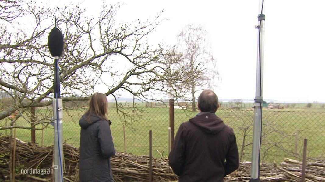 Zwei Anwohner stehen in ihrem Garten und blicken auf das weit entfernte LNG-Terminal in Lubmin