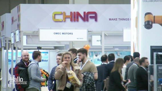 Blick durch einen Gang auf einer Messe mit mehreren Besuchenden und einem Stand mit der Aufschrift "CHINA". © Screenshot 